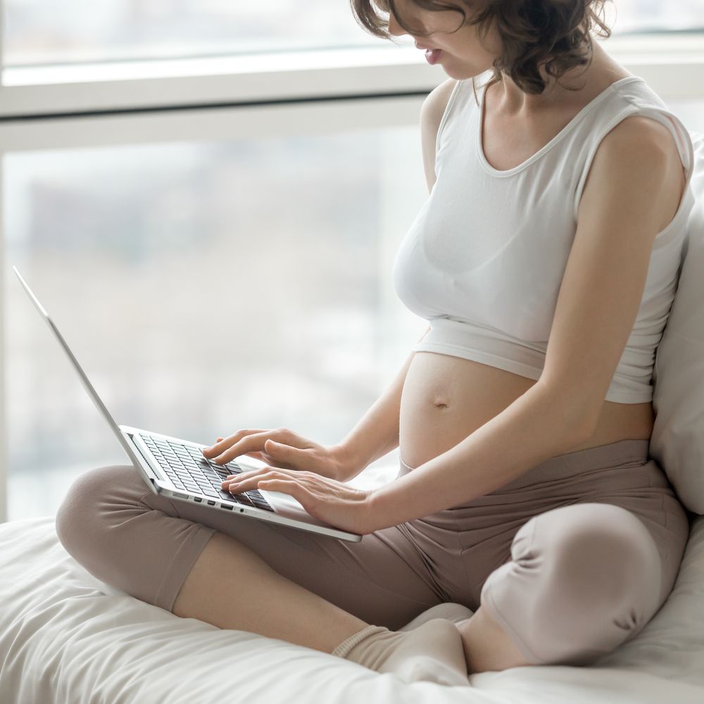 Pregnant woman sitting on bed with laptop computer