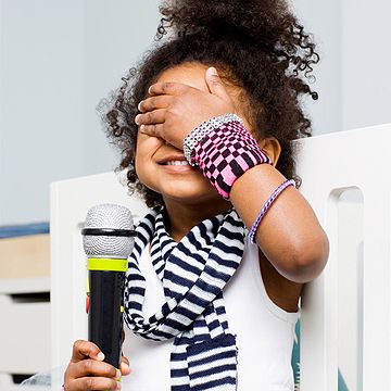 child covering her eyes holding microphone