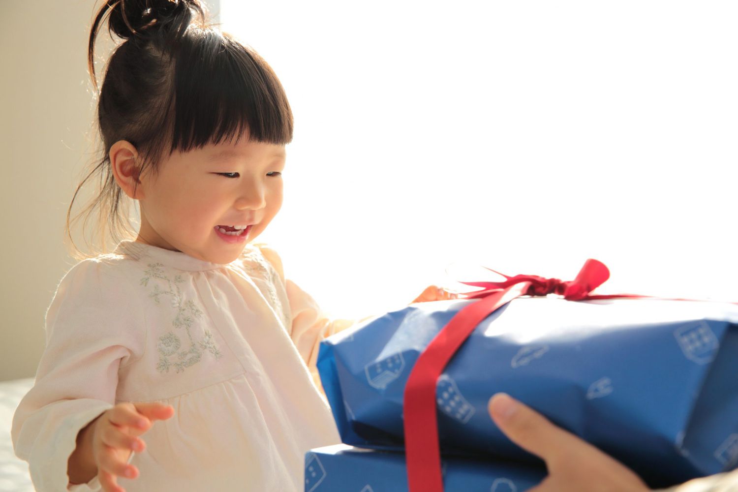 Father giving present to 2 years old daughter on bed in the morning of her birthday in Fukuoka.