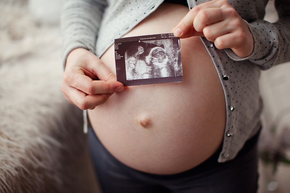 pregnant woman holding ultrasound image on belly