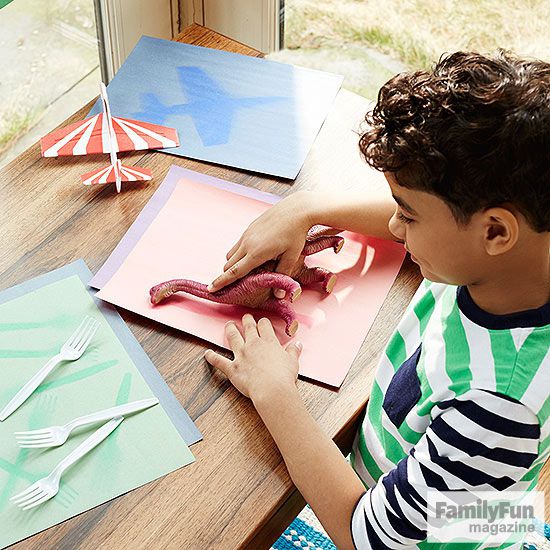 Boy in striped shirt printing dinosaur toy on piece of construction paper
