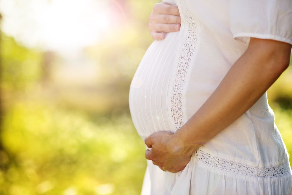 Pregnant woman in white dress holding belly