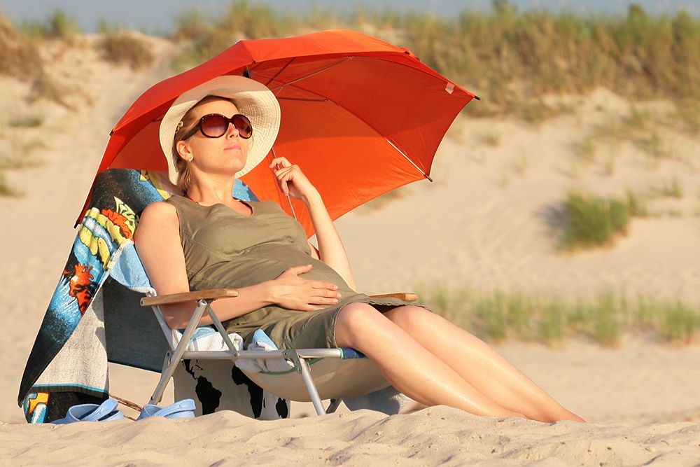 pregnant woman on beach in sun hat and glasses