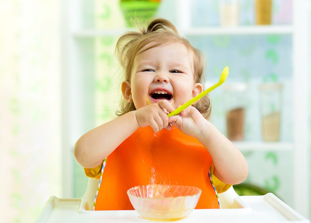 laughing baby eating with spoon