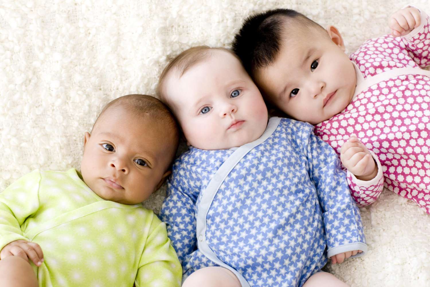 Three babies wearing colorful onesies