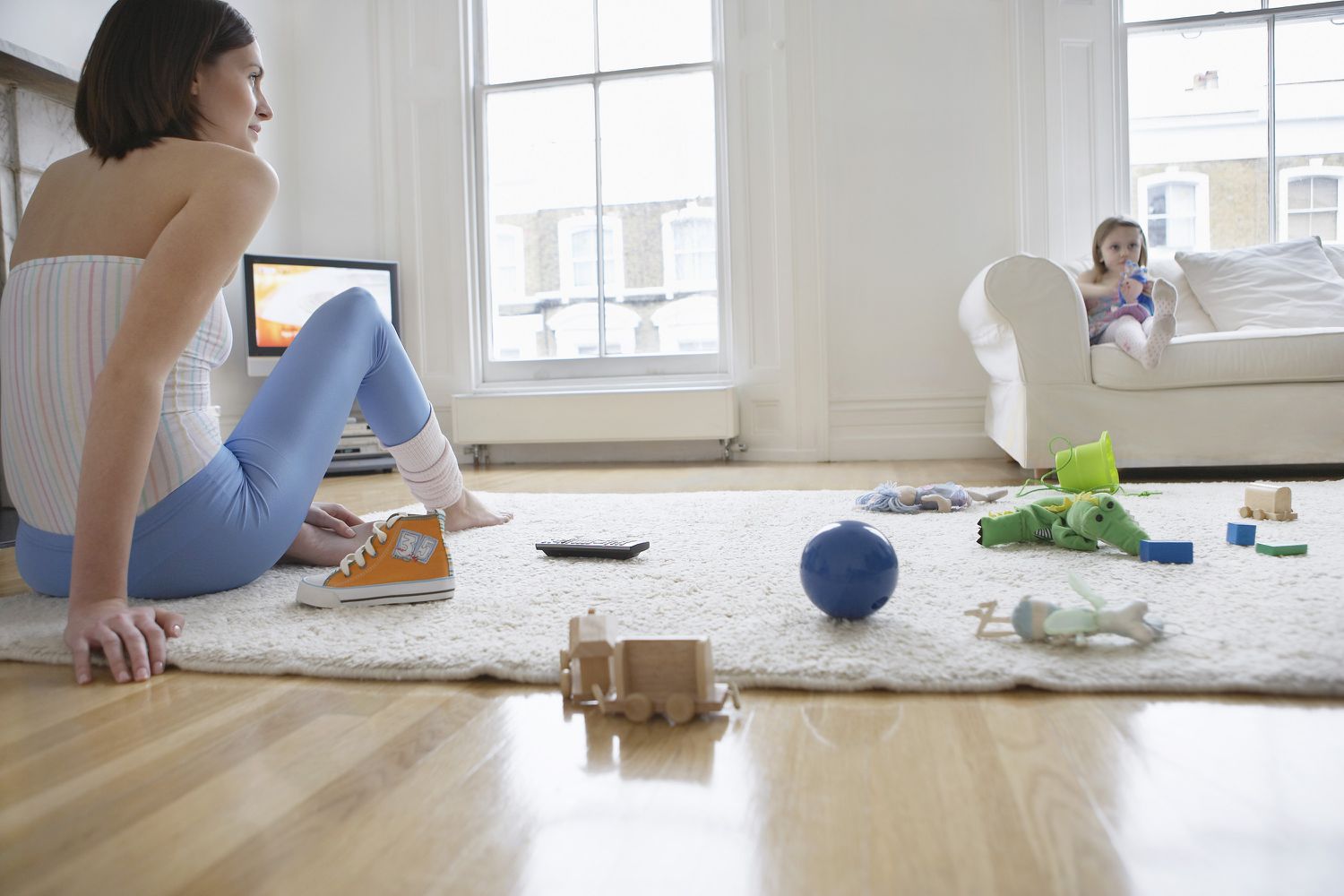 Mom Sitting On Messy Floor of Toys With Daughter on Couch