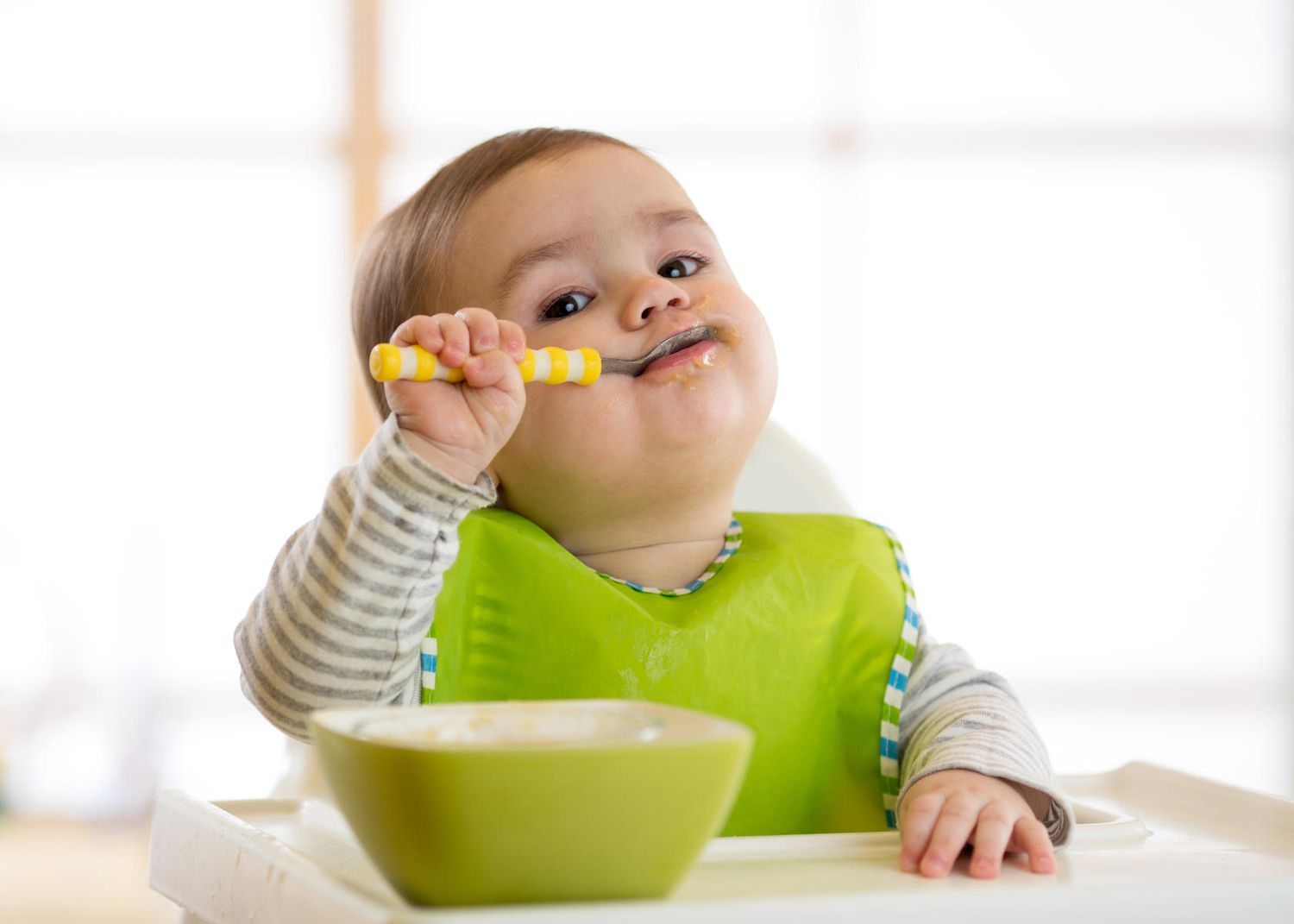 Baby in Highchair Feeds Self With Spoon