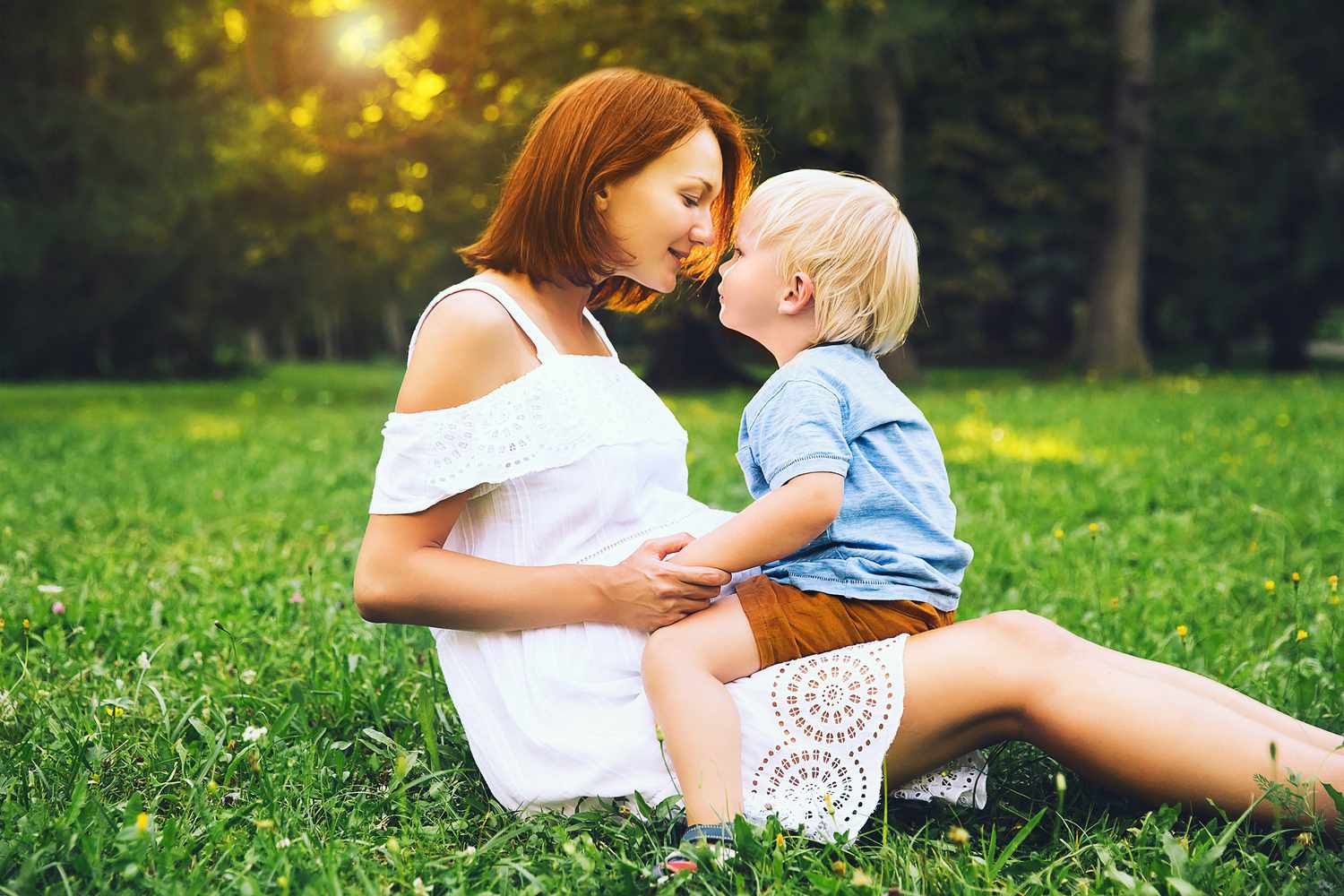 Pregnant Woman and Toddler Son Sitting in Grass Outside Sunlight