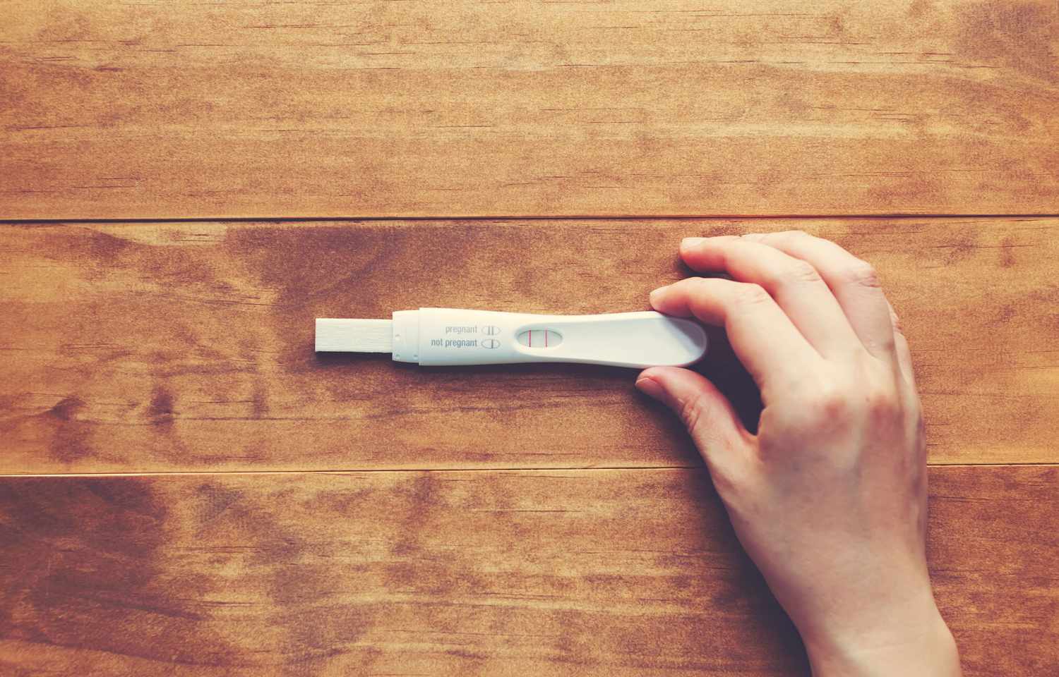Hand Holds Positive Pregnancy Test on Wooden Table