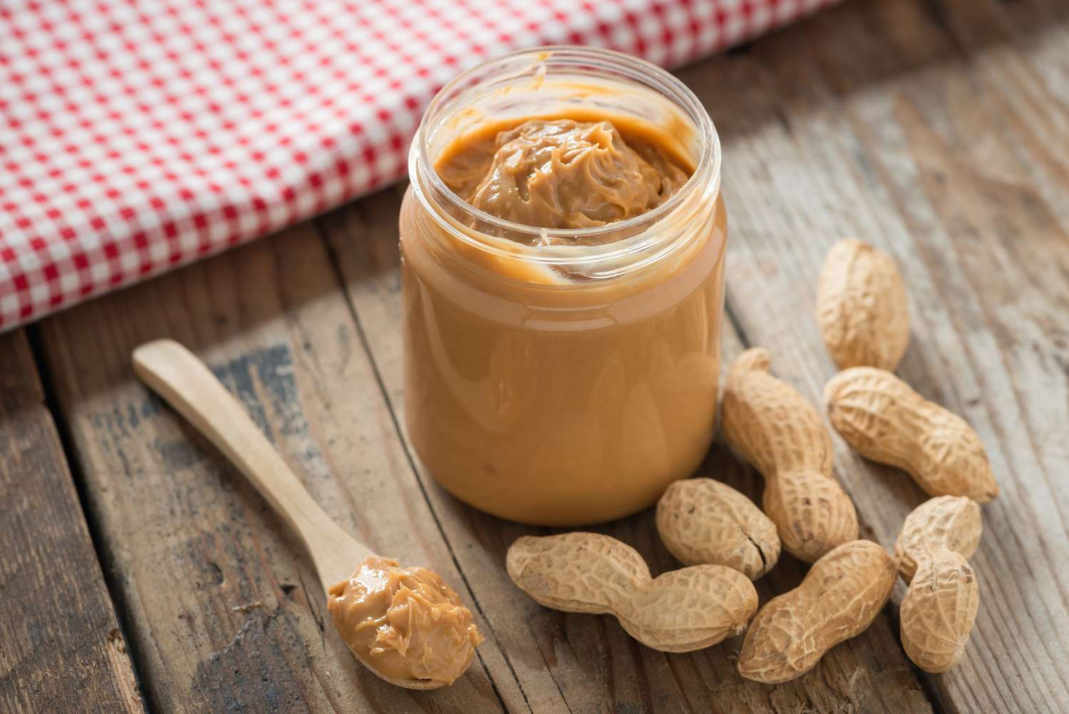 Jar of Peanut Butter Creamy and Whole Peanuts on Table