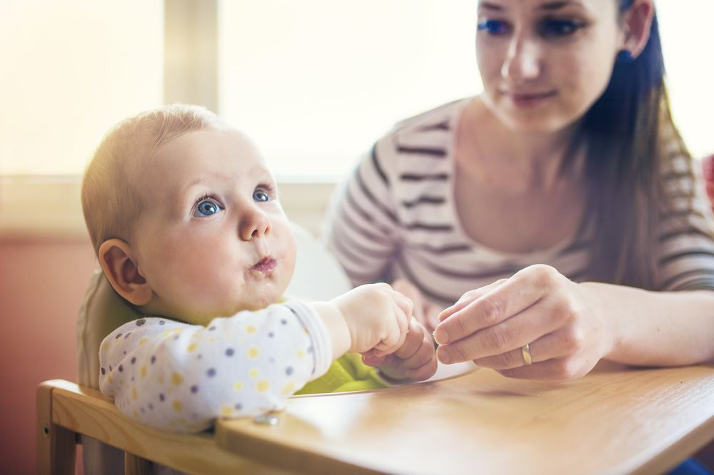 young mom feeding baby in high chair