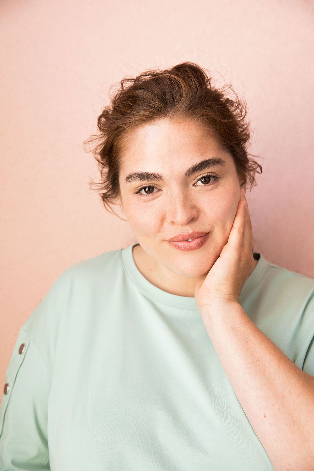woman in muted green shirt against pink backdrop