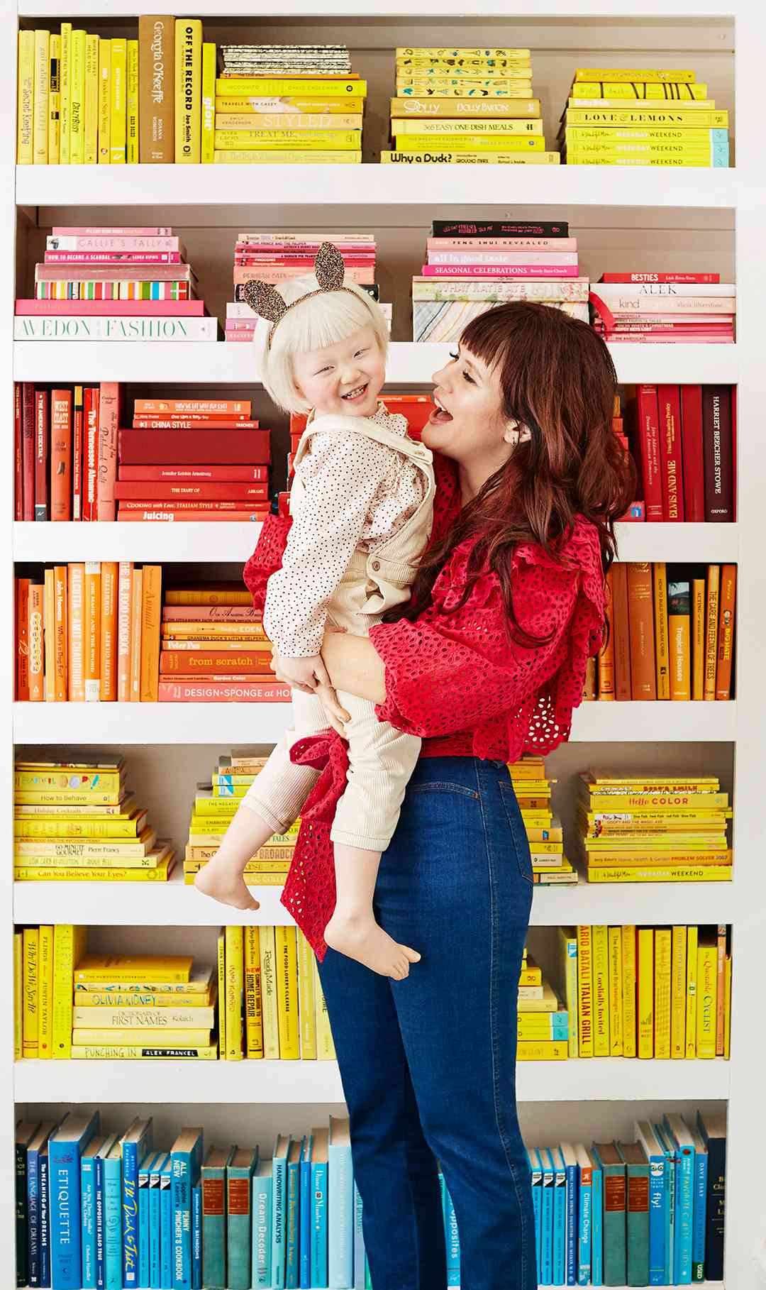 mother holding daughter in front of color coordinated book shelf