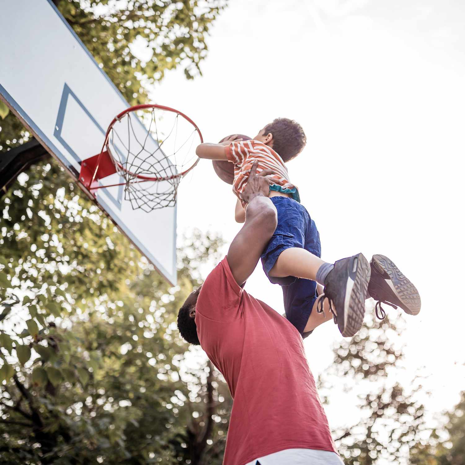 father lifting son so he can put basketball in basket