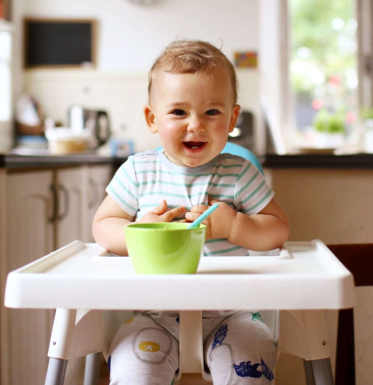 A 1 year old boy smiling on his high chair