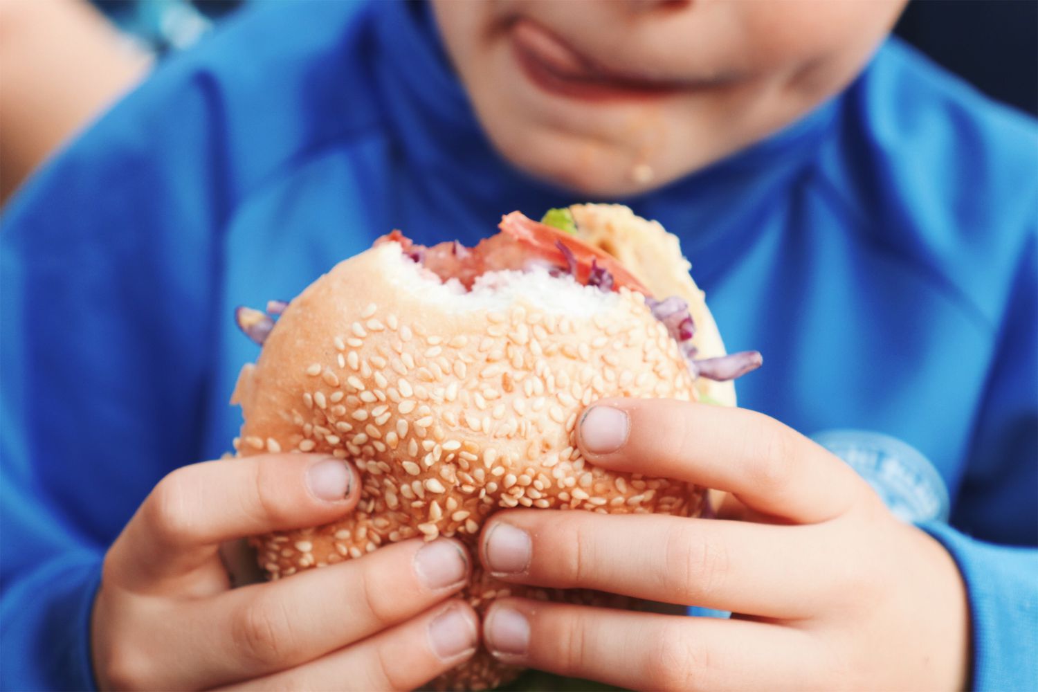 Midsection Of Boy Holding Burger Licking Lips