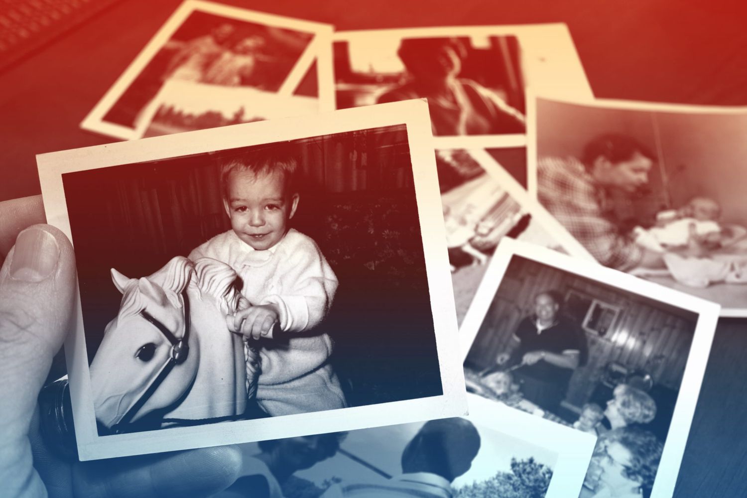 Hand holds Vintage photograph of child on horse toy with pile of old photos in background