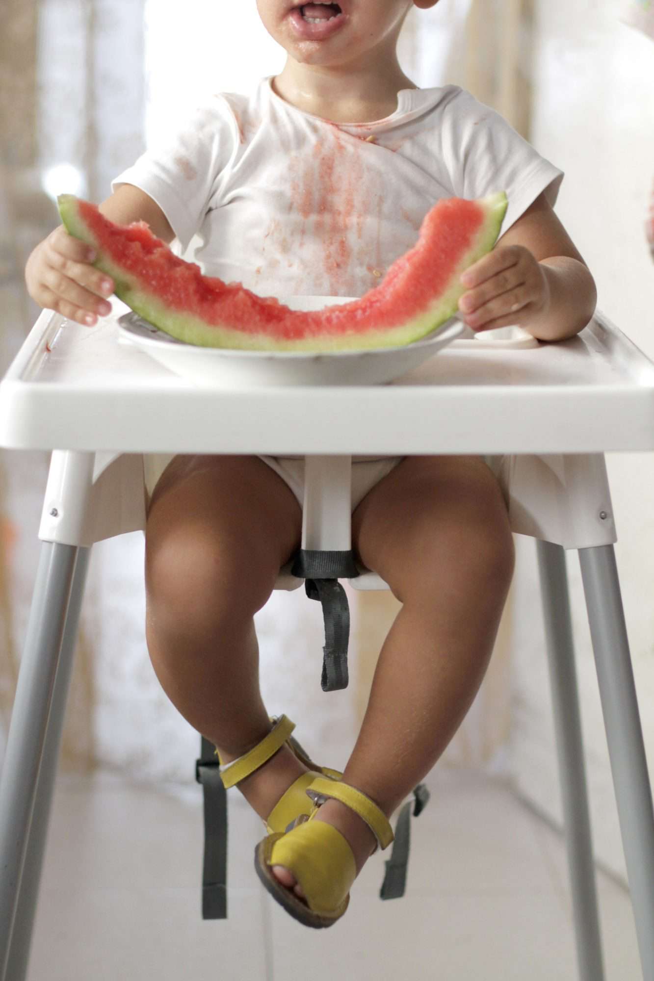 Baby boy eating a slice of watermelon on high chair
