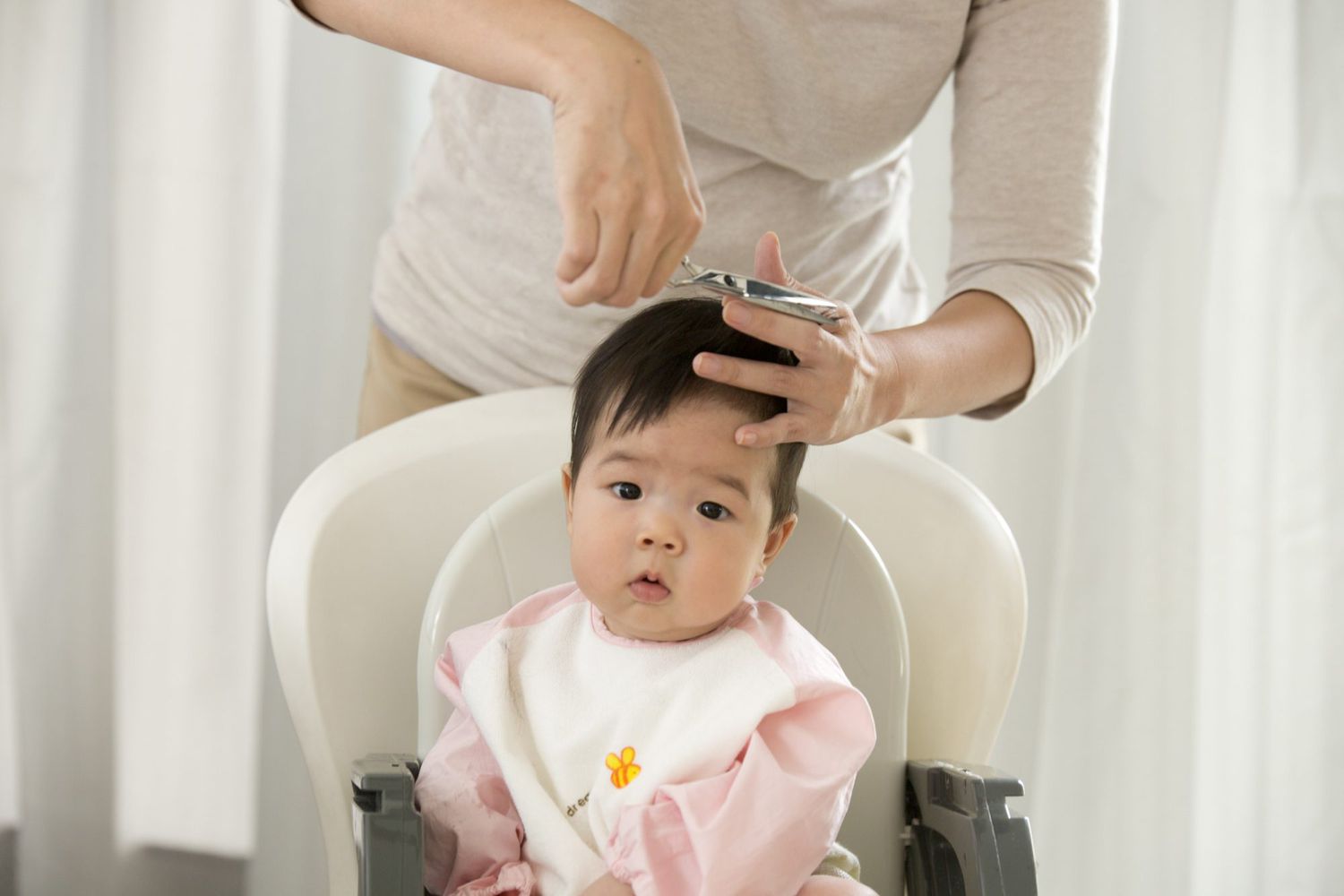 Asian toddler sitting in highchair while mother trims hair