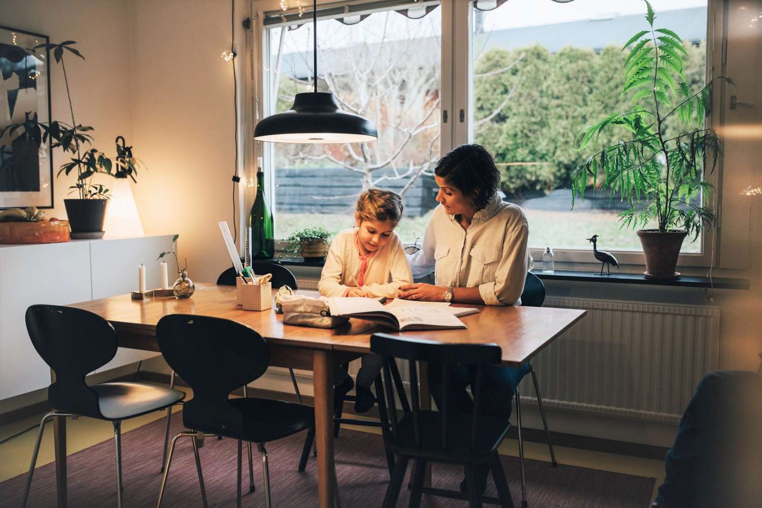 Mother assisting daughter in writing homework while sitting at home