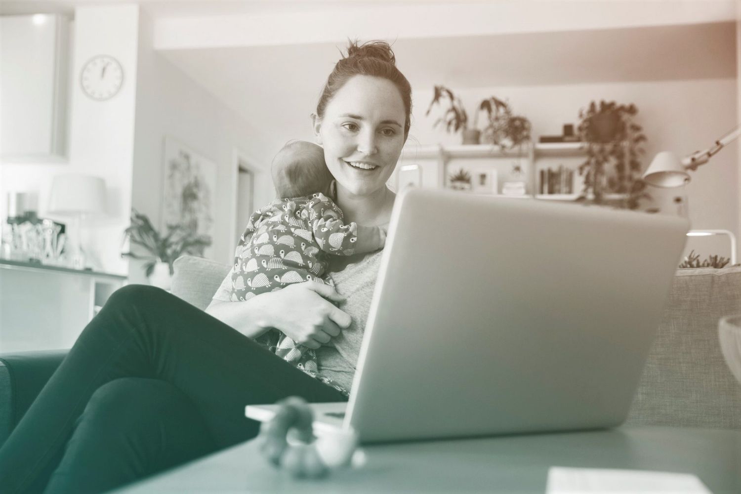Mother using laptop and holding her newborn baby at home