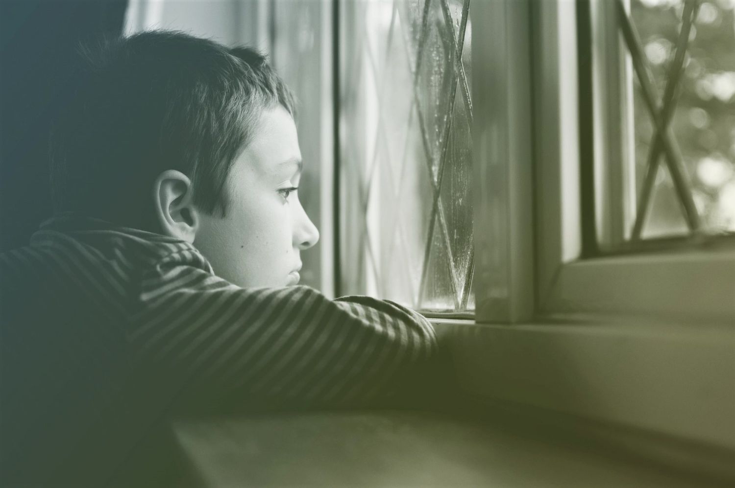 Young boy looking out window on rainy day