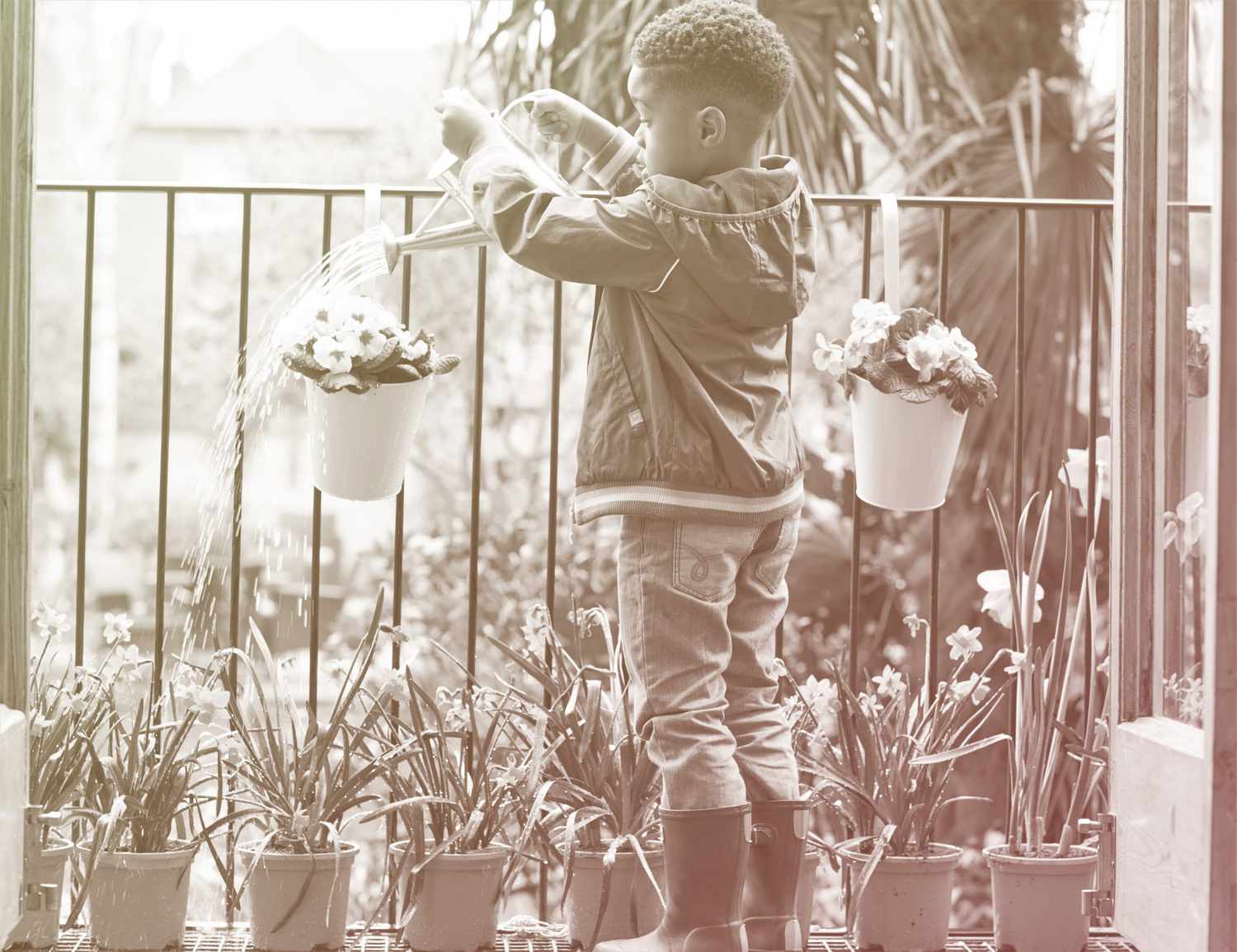 young boy watering potted plants on balcony