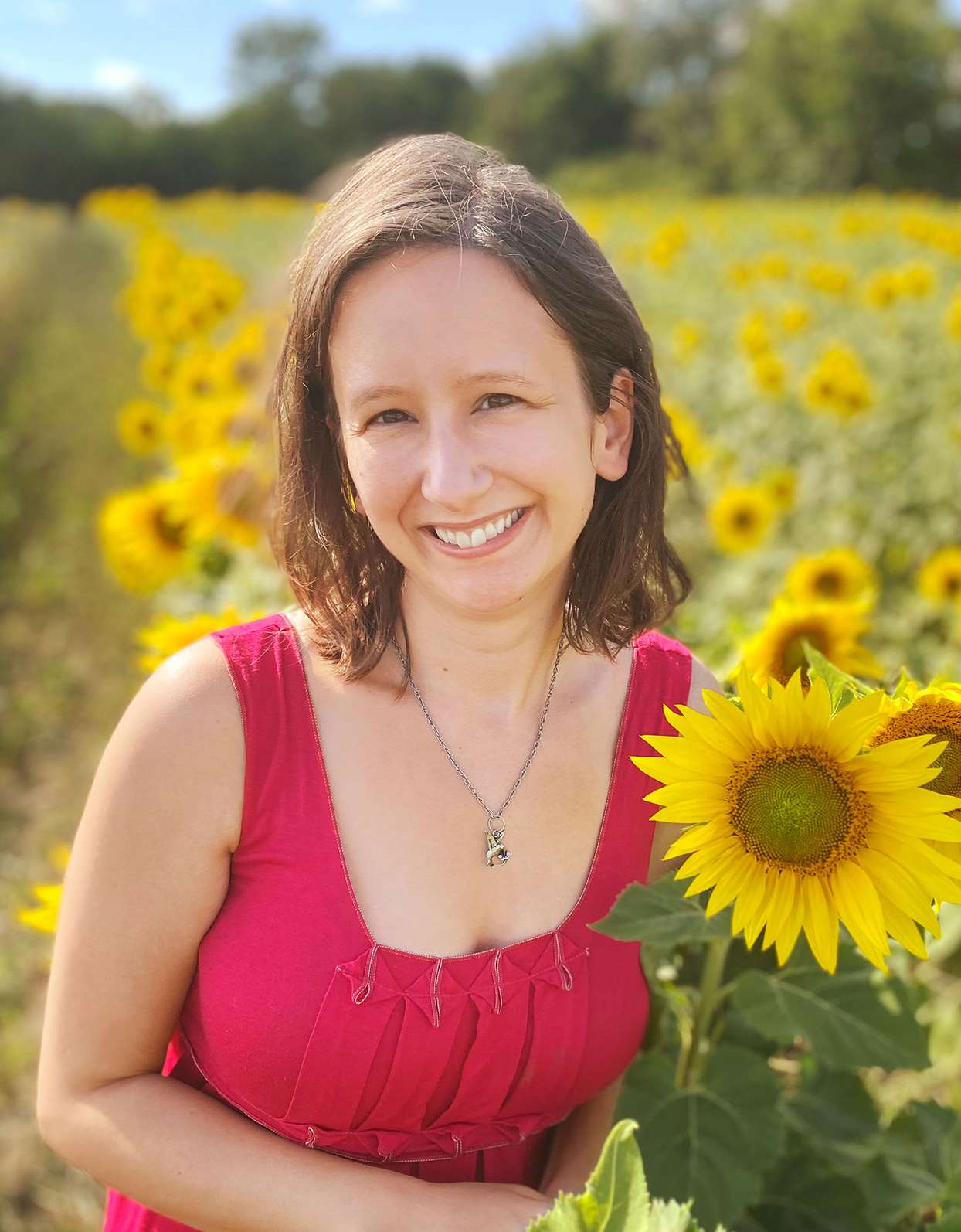 woman in red dress smiling in field of sunflowers