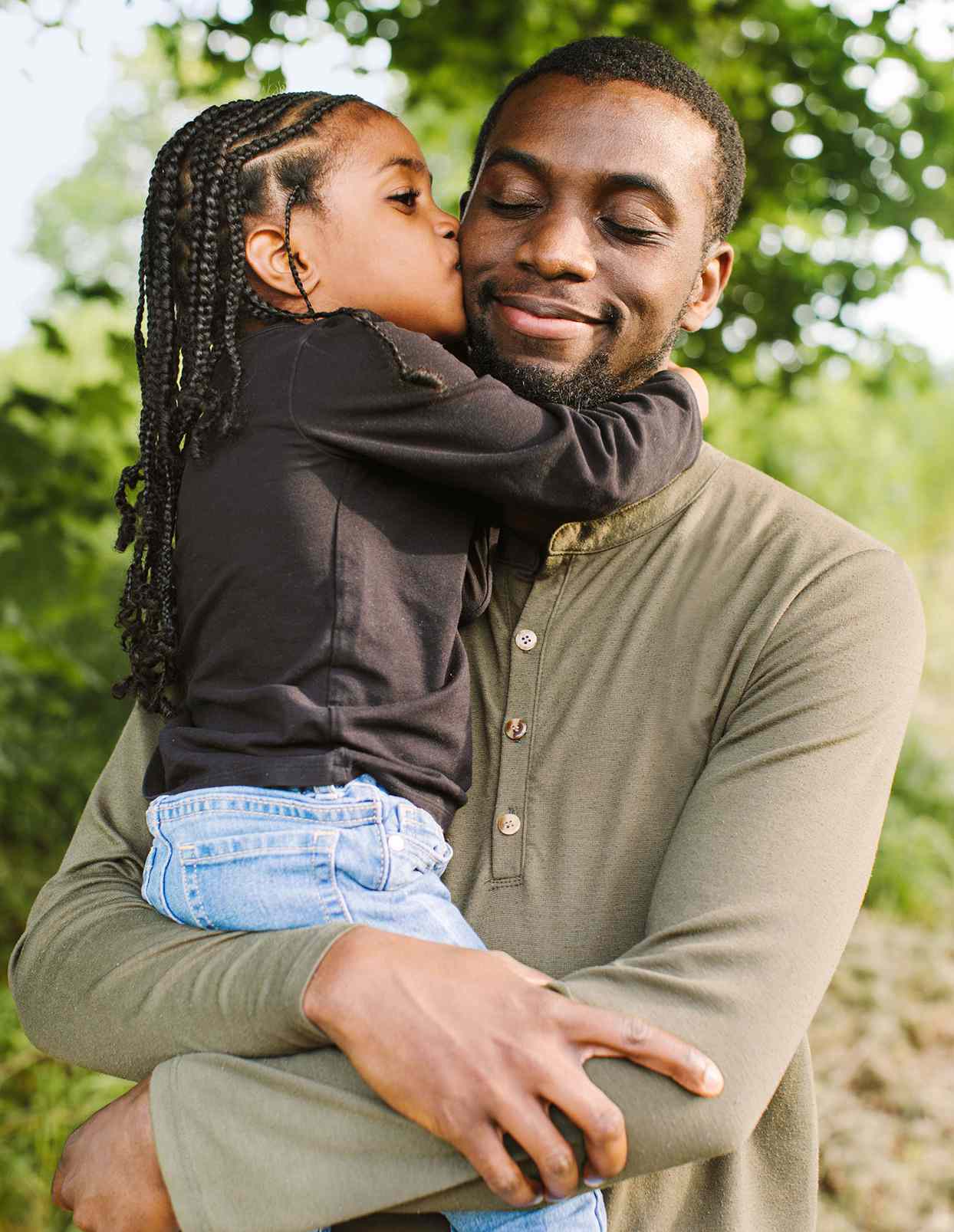 young son in his smiling father's arms outside kissing his cheek