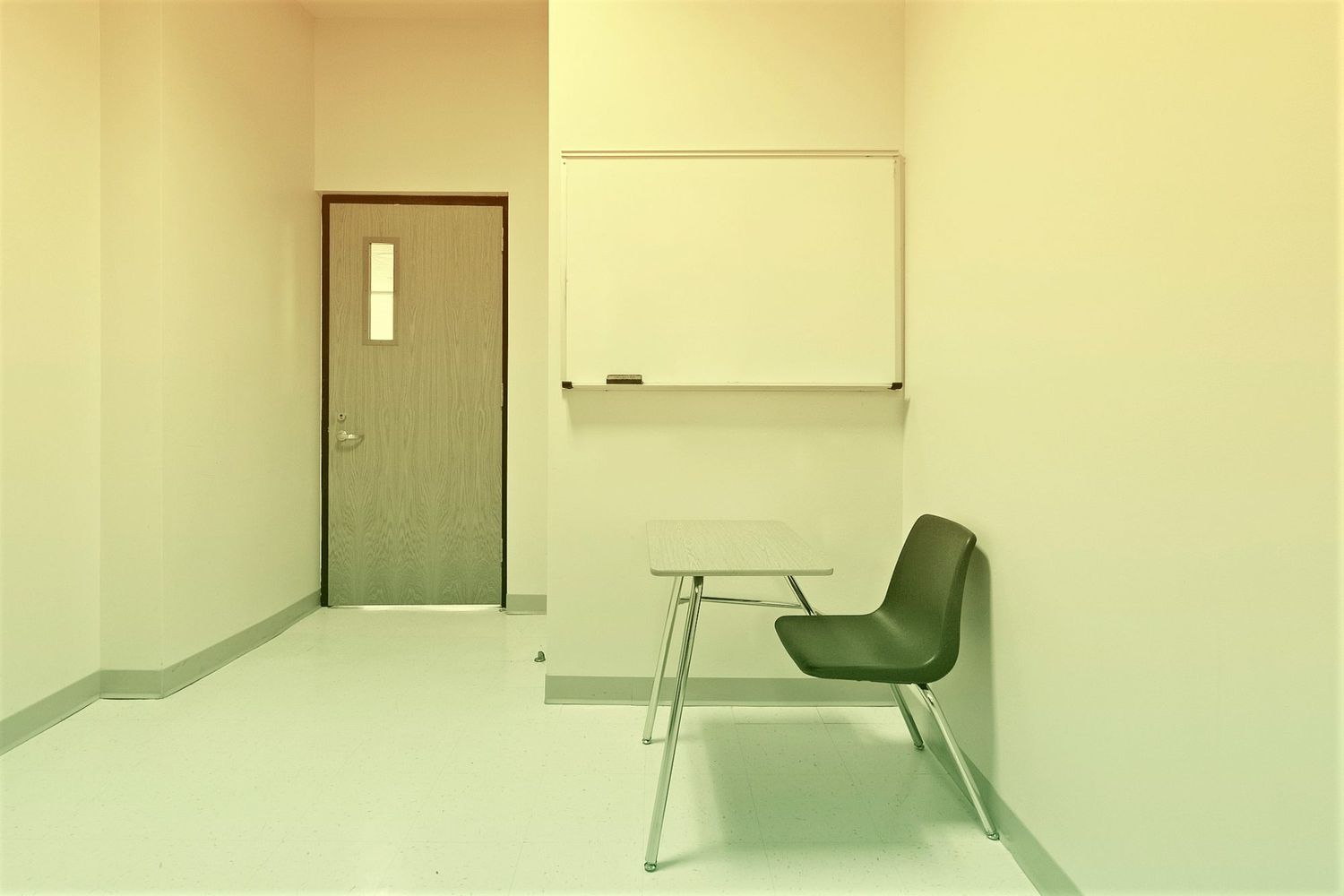 a school chair and desk in an empty room with a dry erase board on the wall and an entrance door