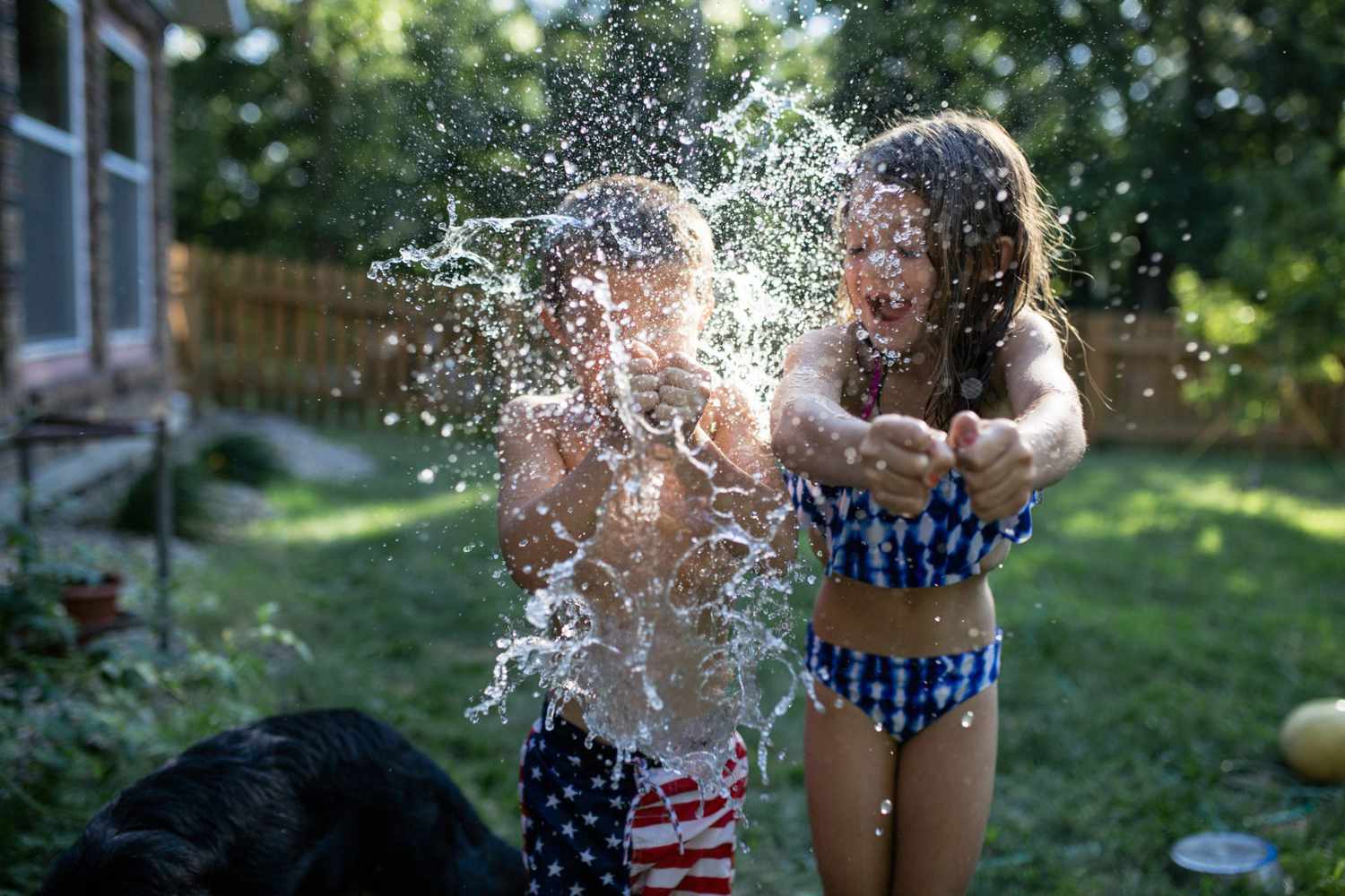 An image of siblings bursting water balloons in a backyard.