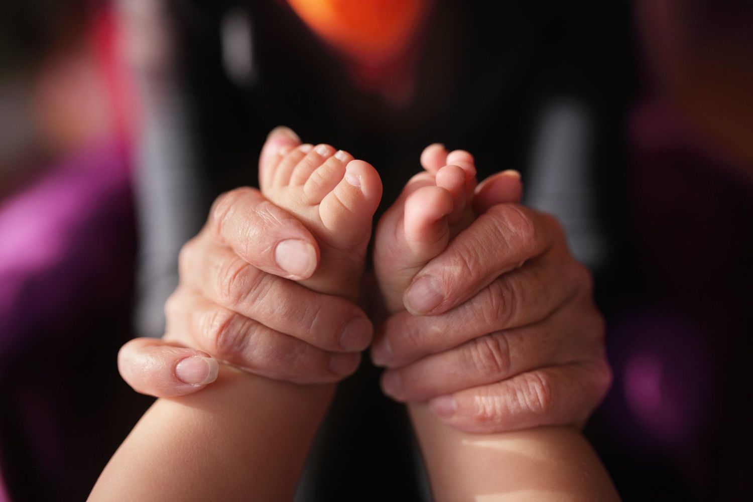 An image of the hands of a grandmother holding a newborn baby's feet.