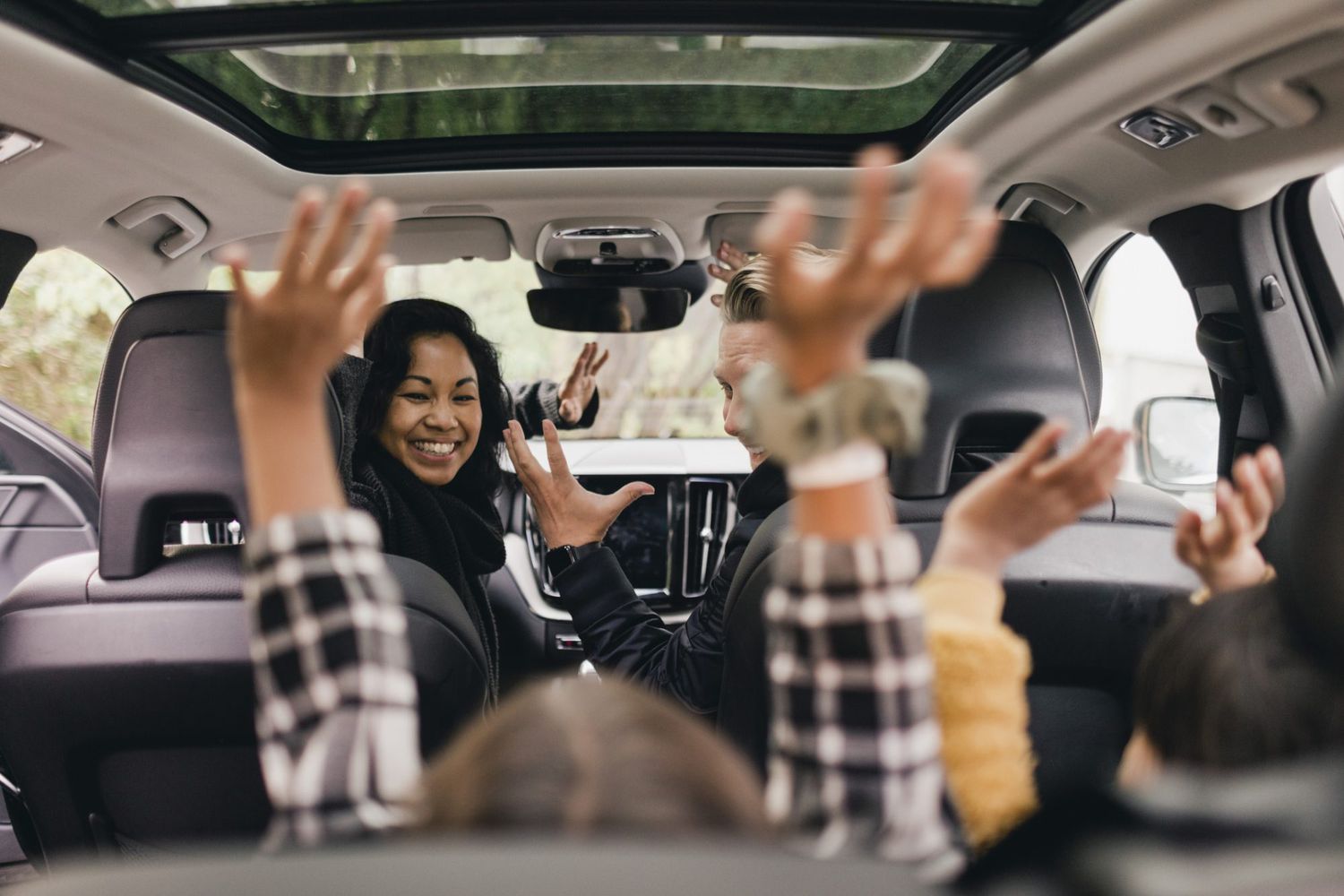 An image of a family raising their hands while on a road trip.
