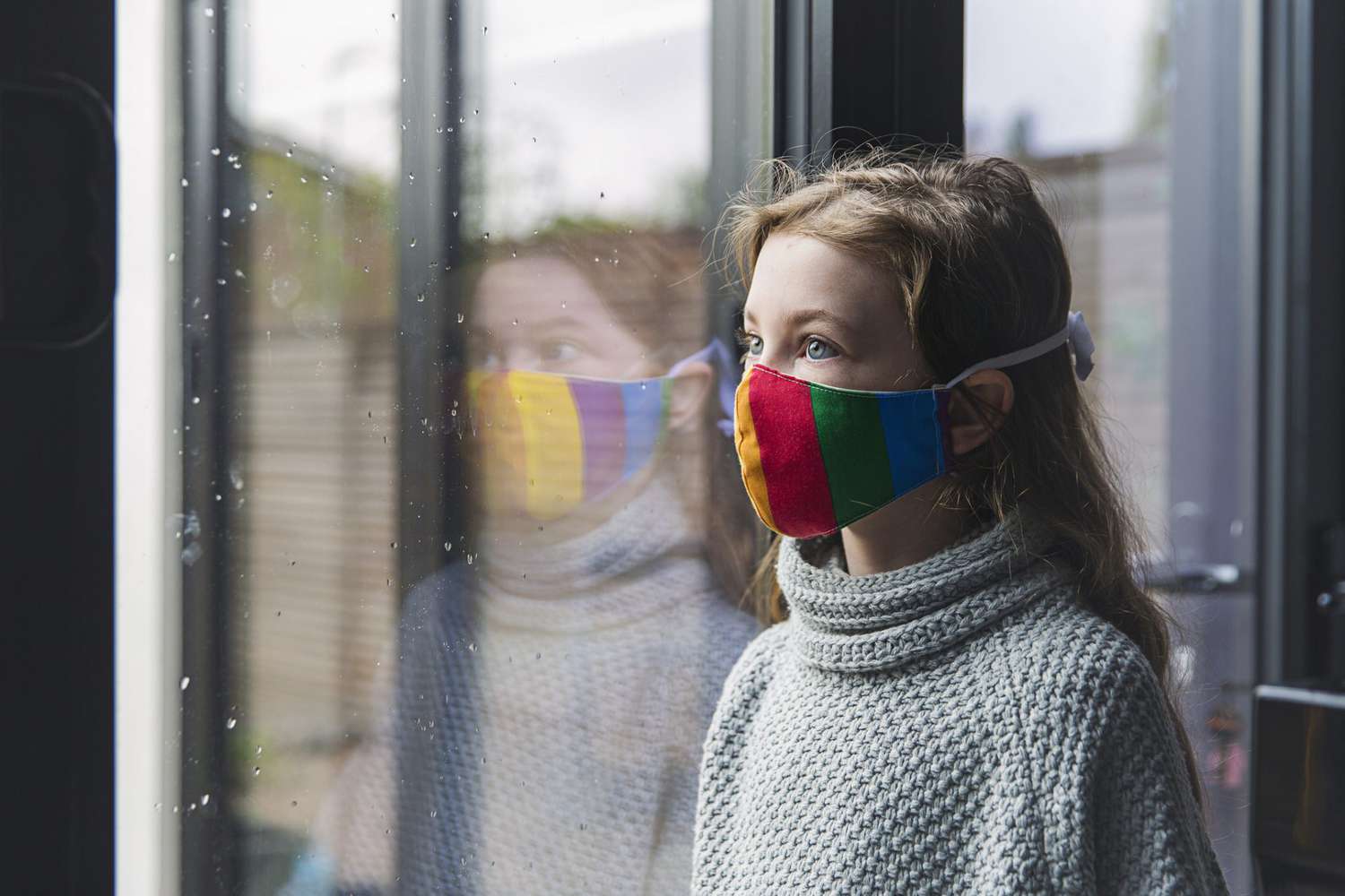 An image of a girl wearing a mask looking out a window.