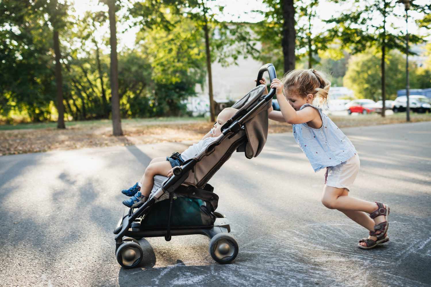 An image of a child pushing a toddler in a stroller.