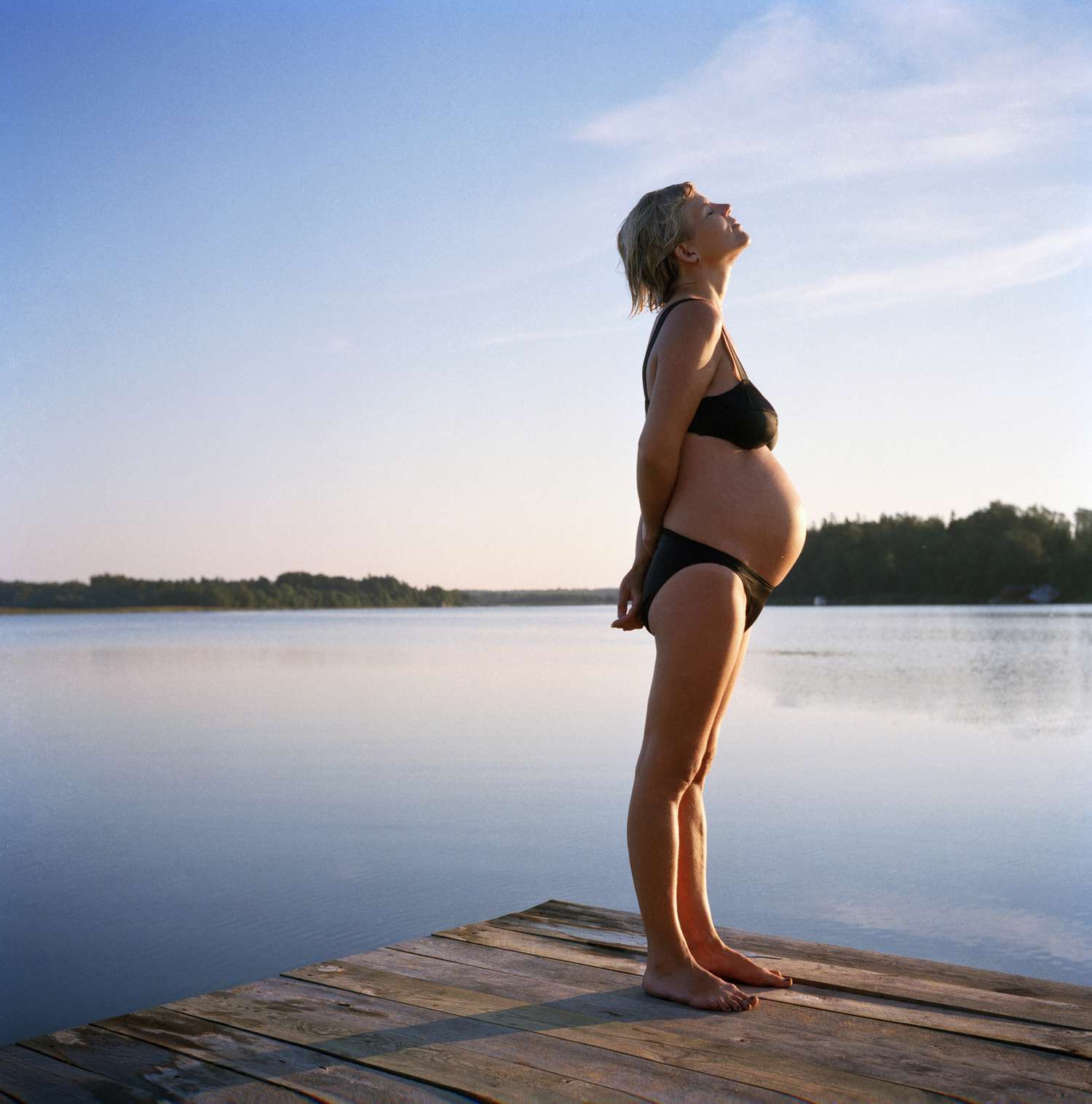 An image of a pregnant woman standing on a jetty at lake