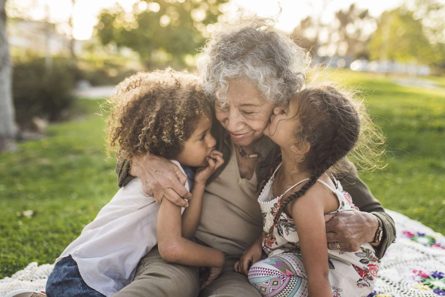 An image of grandchildren with their grandmother on a picnic blanket at a park.