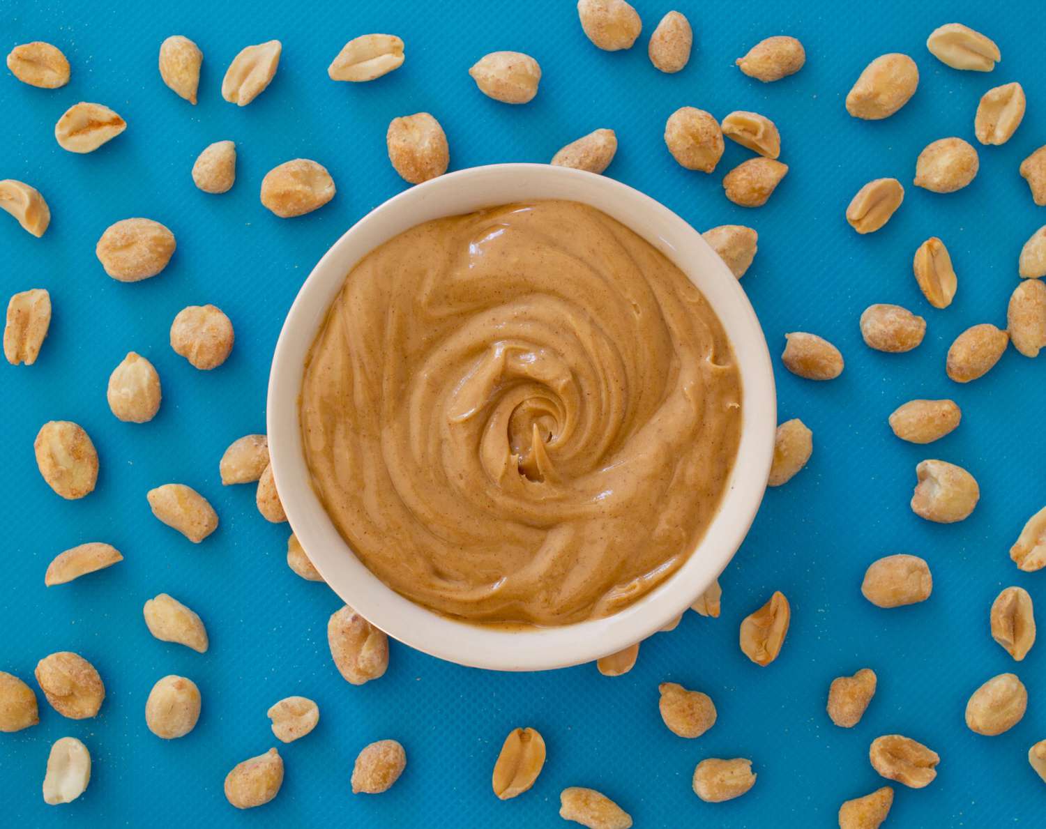 An image of peanut butter and peanuts on a blue background.