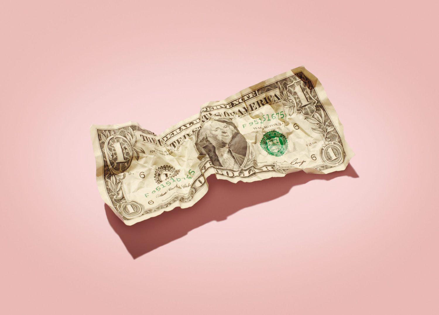 An image of a crumpled dollar bill on a pink background.