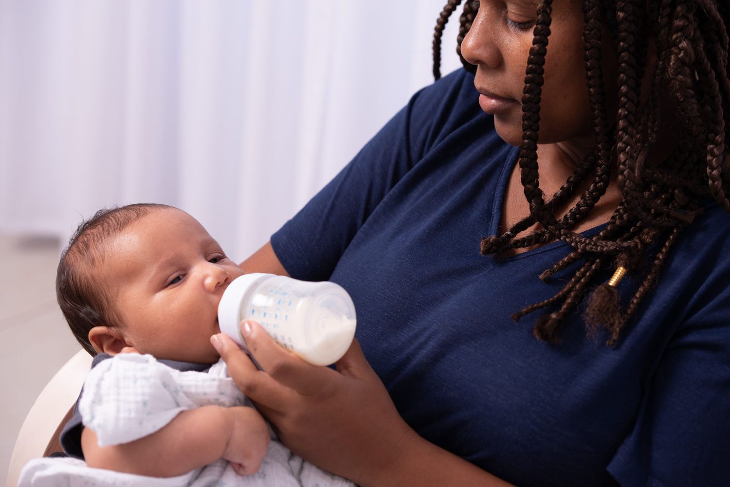 Close-up image of a doula feeding baby girl with the bottle