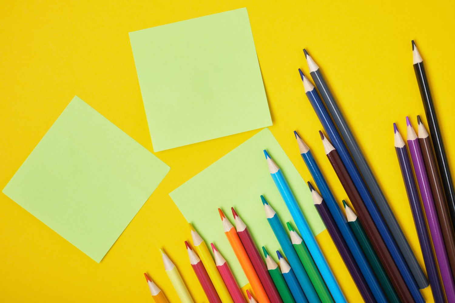 An image of colored pencils and sticky notes on a yellow background.