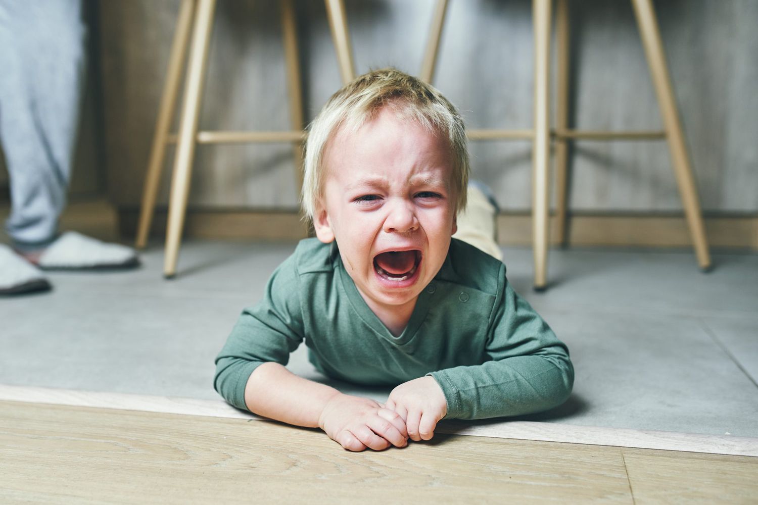 A little boy with blond hair, two years old, is lying on the floor and crying hysterically