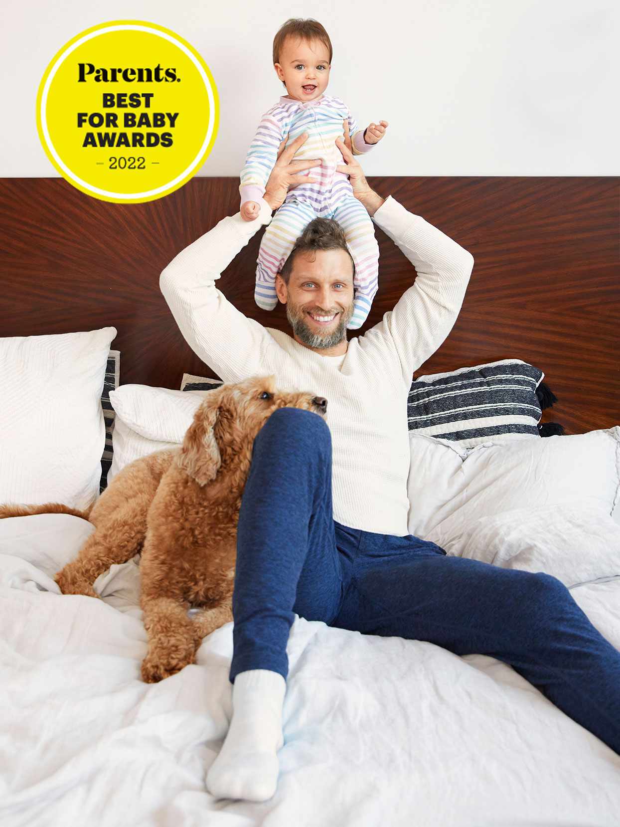 happy father lifting baby in bed dog