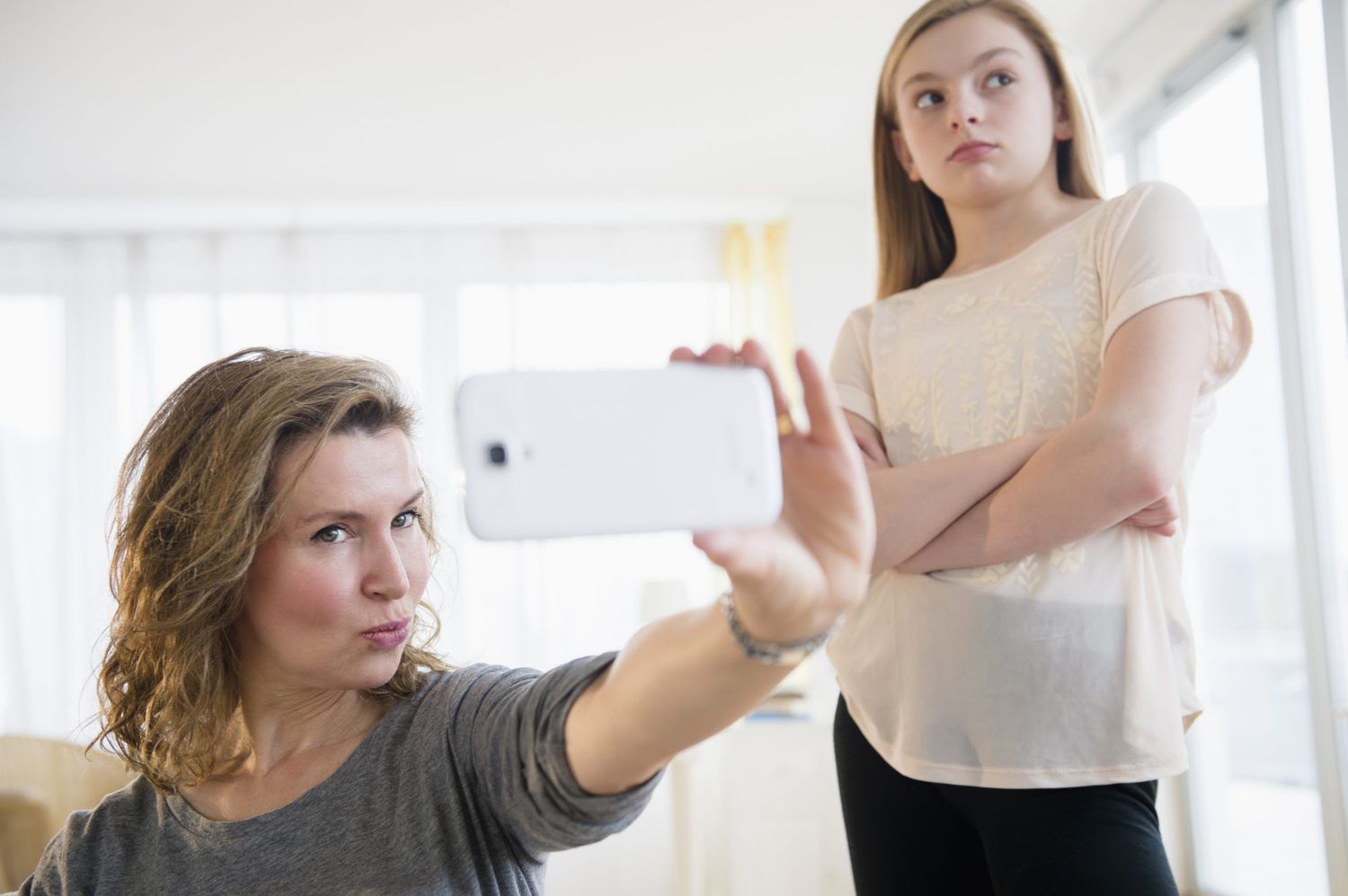 Mom taking a selfie, teen in background looking embarrassed
