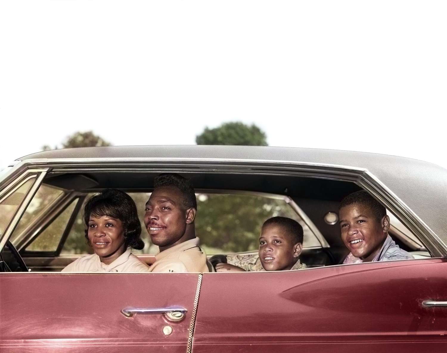 1960s SIDE VIEW OUTDOOR SMILING AFRICAN AMERICAN FAMILY FATHER MOTHER TWO SONS SITTING IN FOUR DOOR SEDAN AUTOMOBILE