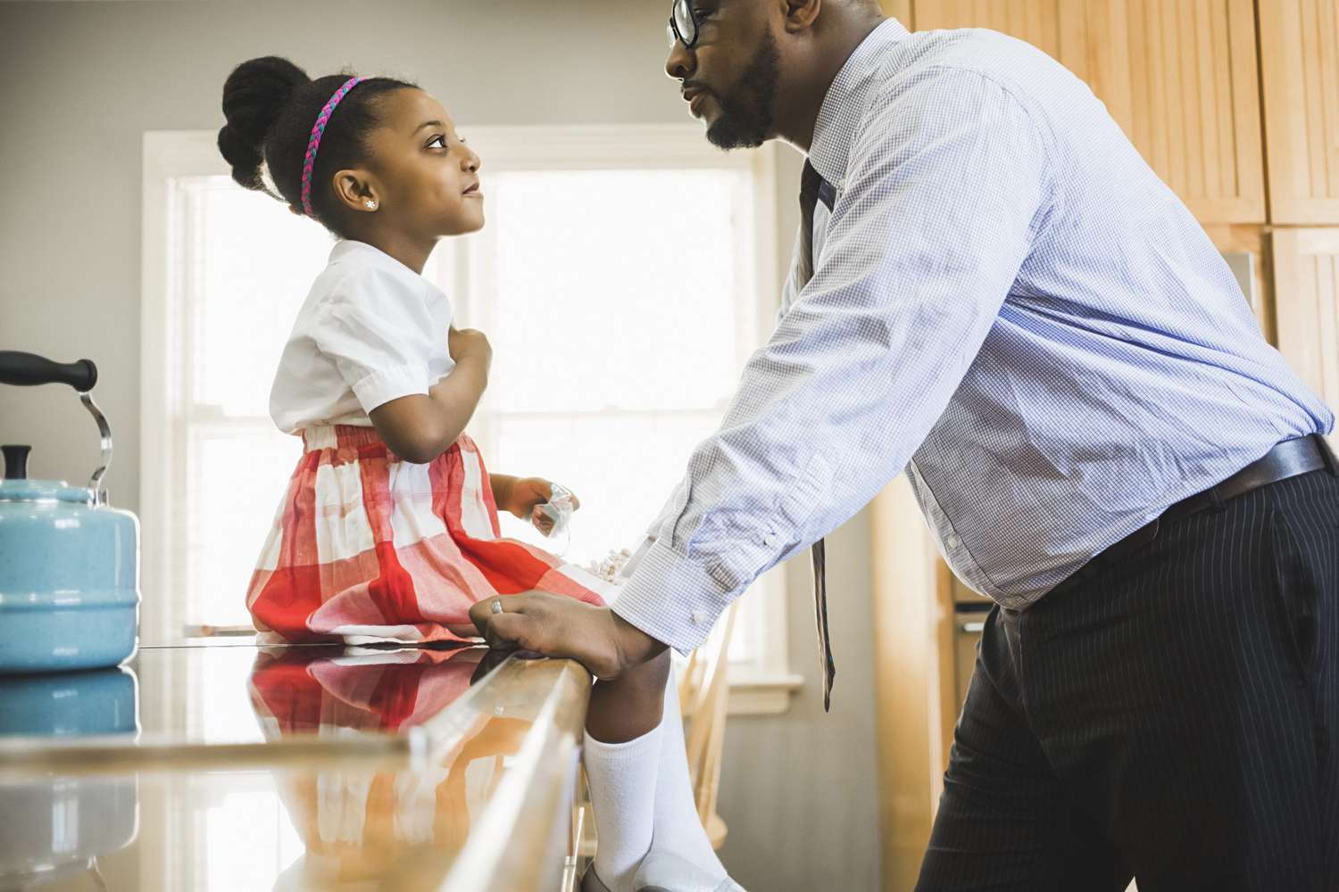 Side view of father and daughter talking in kitchen during morning