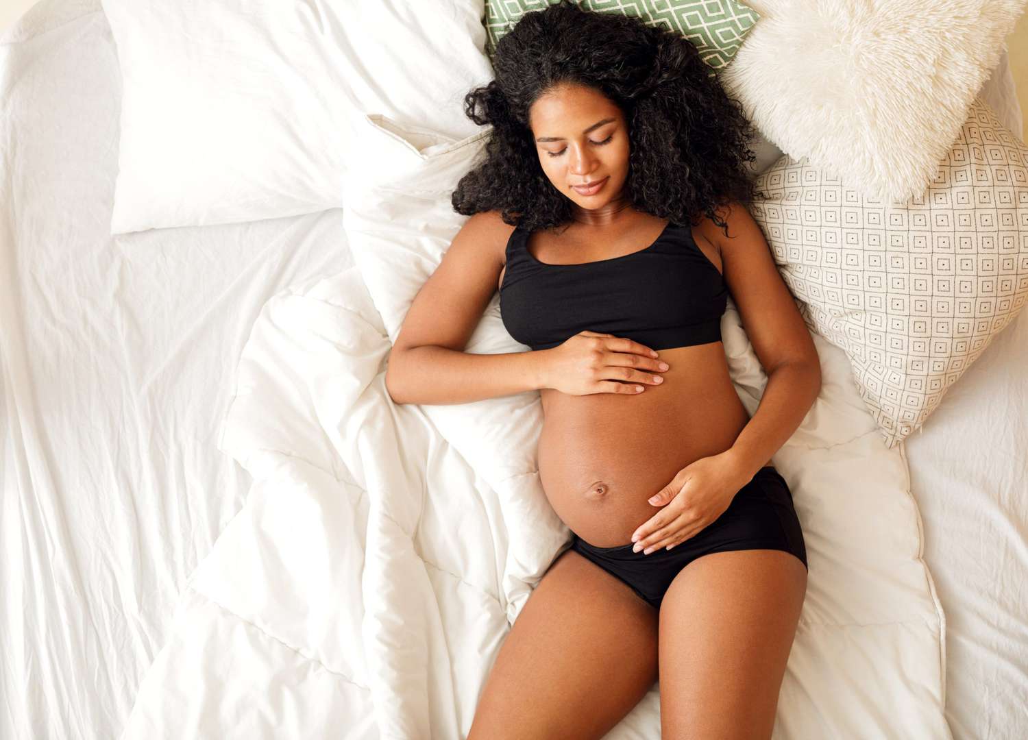 High angle view Of pregnant Black woman lying on bed holding her belly