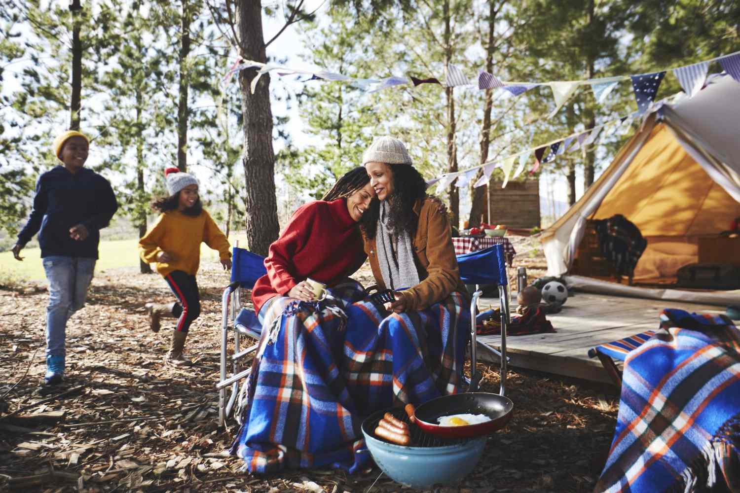 Happy lesbian couple with kids relaxing at campsite in woods