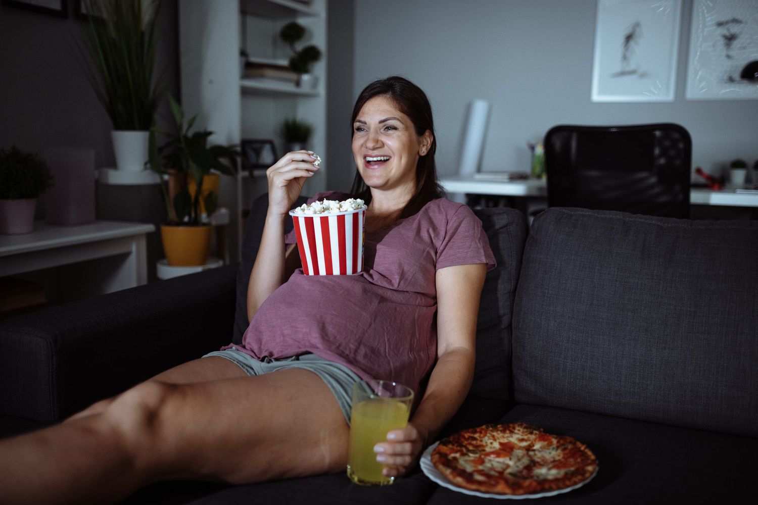 Pregnant woman eating junk food and watching TV - overeating during pregnancy