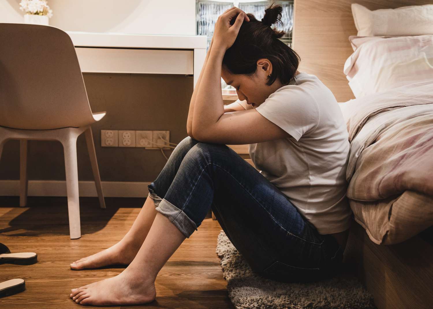 Asian woman sitting on floor next to bed feeling depressed